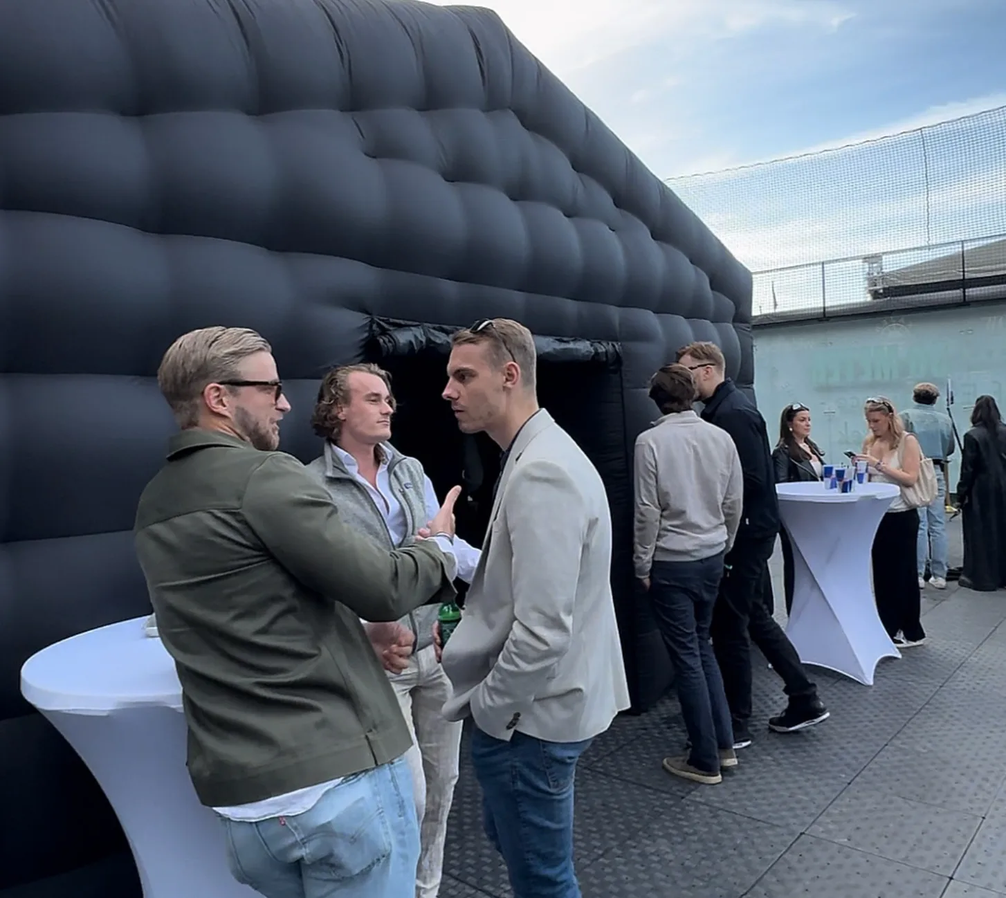 Gäster minglar vid vita ståbord utanför ett svart uppblåsbart partytält på en stenlagd uteplats